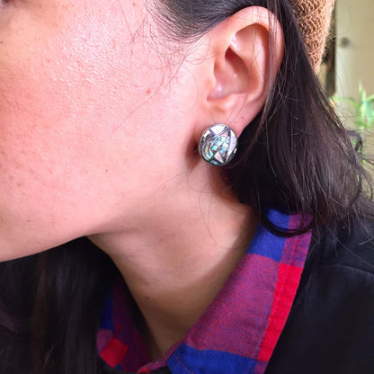 Closeup of a woman's ear wearing a vintage silver abalone shell earring against a blurred background. The earring features an abalone shell mosaic design on a silver setting.