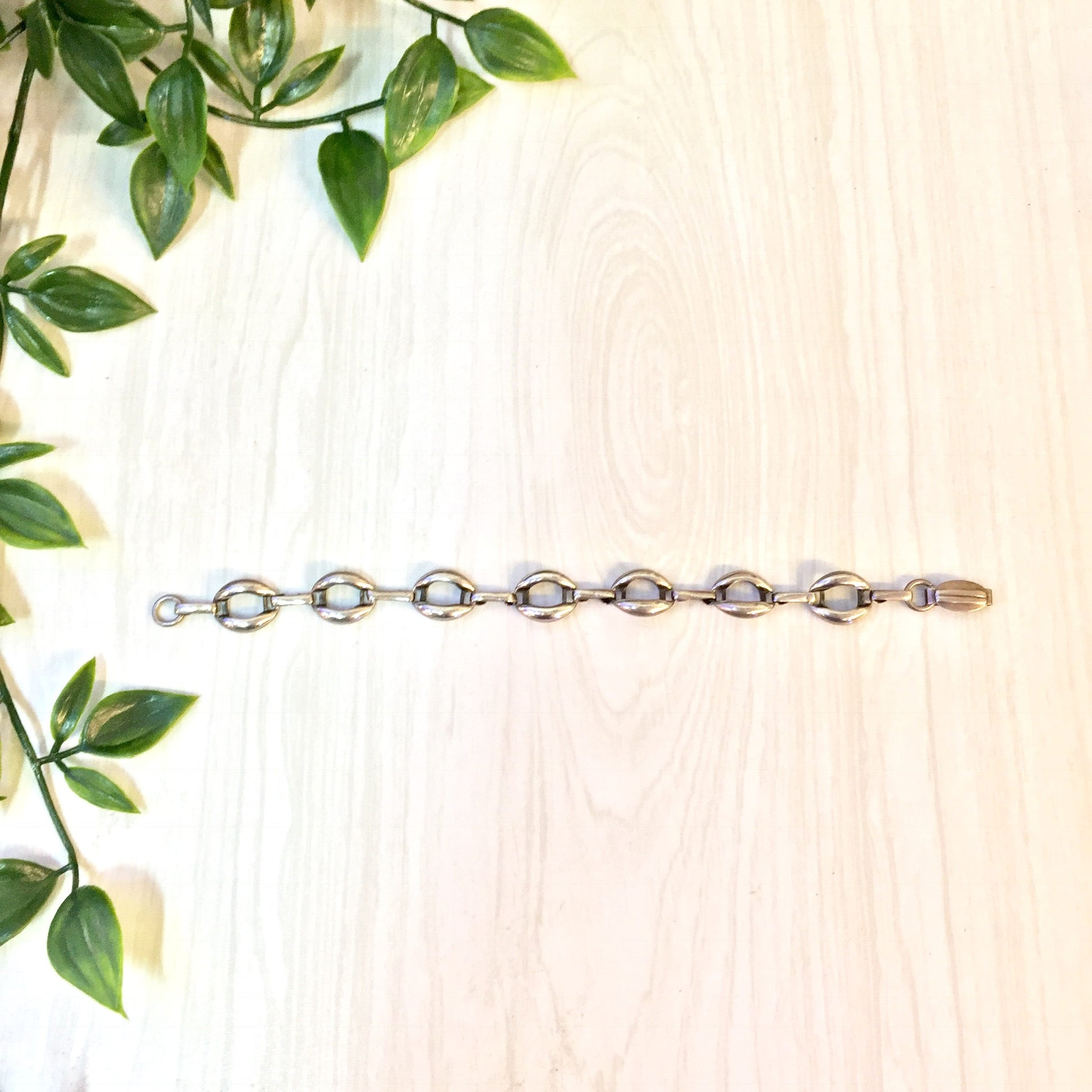 Vintage sterling silver link bracelet with green leaves on wooden background