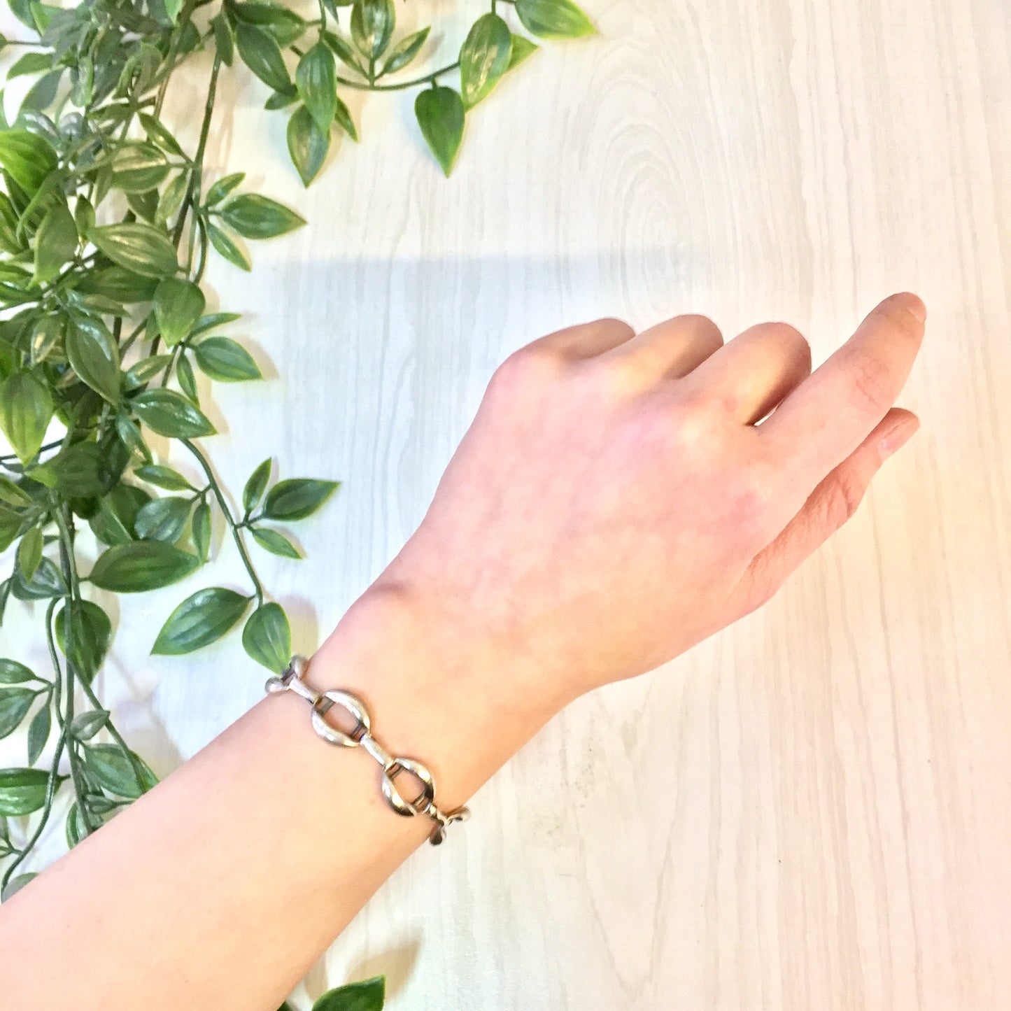 Vintage sterling silver link bracelet on woman's wrist next to plant leaves, simple jewelry gift idea for Valentine's Day or any occasion