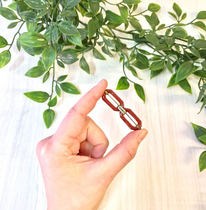 Hand holding a vintage red brooch with carnelian gemstone, set against a leafy green background.