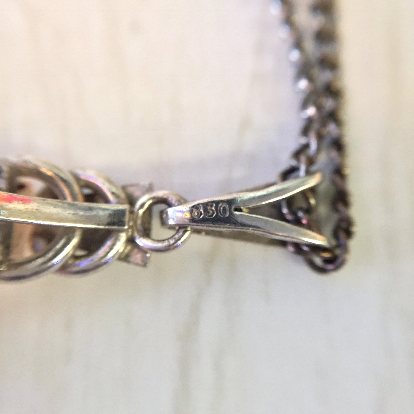 Closeup of vintage Art Deco style silver necklace chain with smoky quartz pendant, showing 930 hallmark on clasp, against blurred light background.