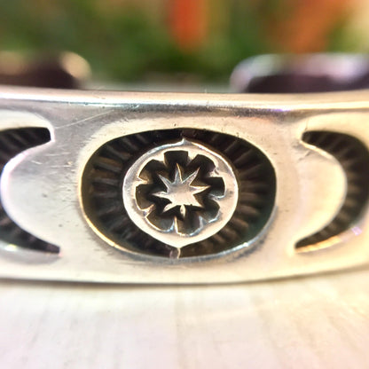 Vintage Hopi silver cuff bracelet with stamped sun, moon and star design, close-up detail view on wooden surface.