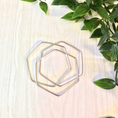 Vintage sterling silver geometric hexagon three-piece bangle bracelet displayed on wooden surface with green plant leaves