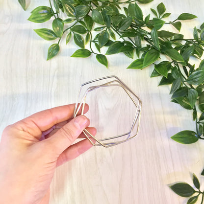 Vintage sterling silver hexagon bangle bracelet held in hand near green foliage