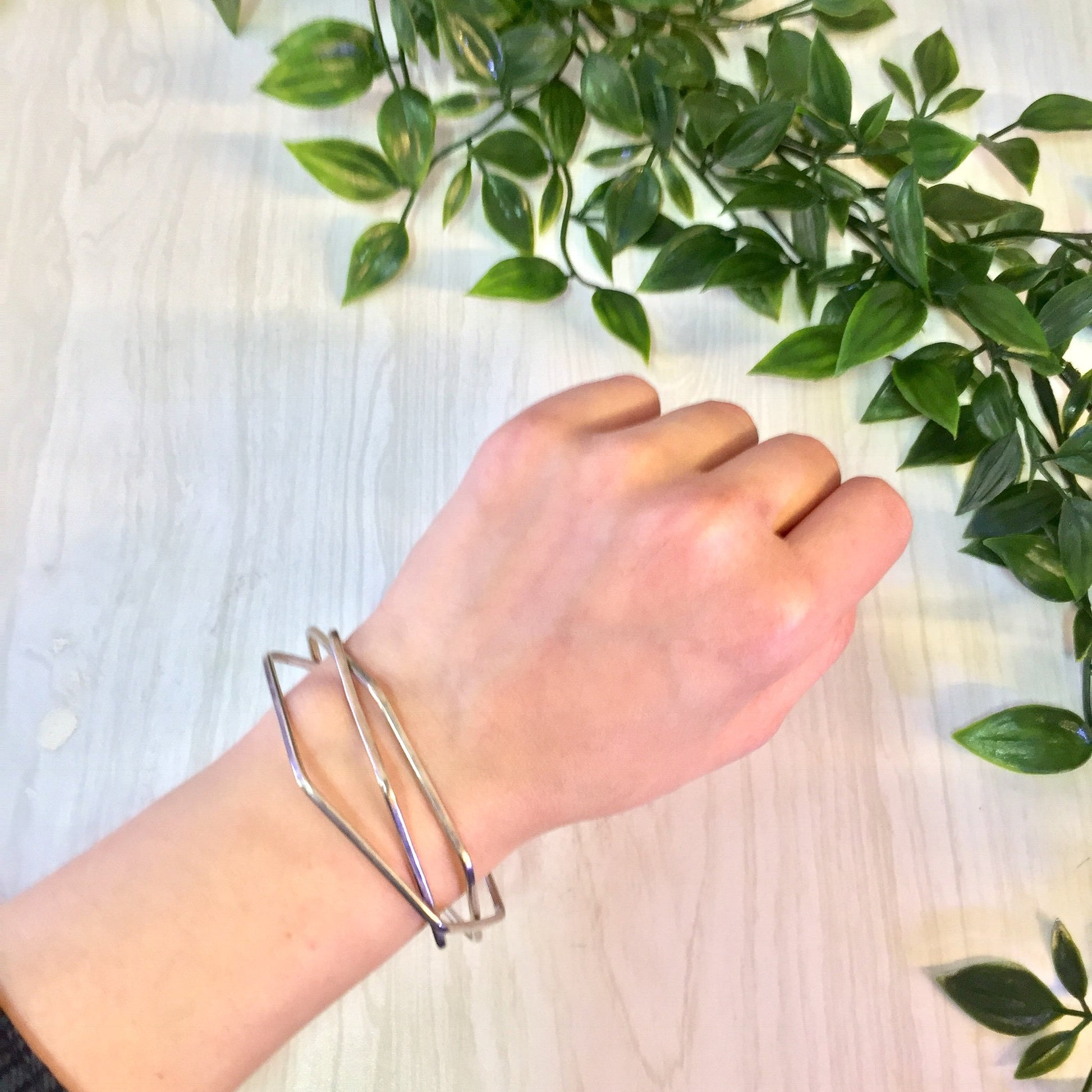 Vintage sterling silver geometric hexagon three-piece bangle bracelet displayed on wrist near green foliage