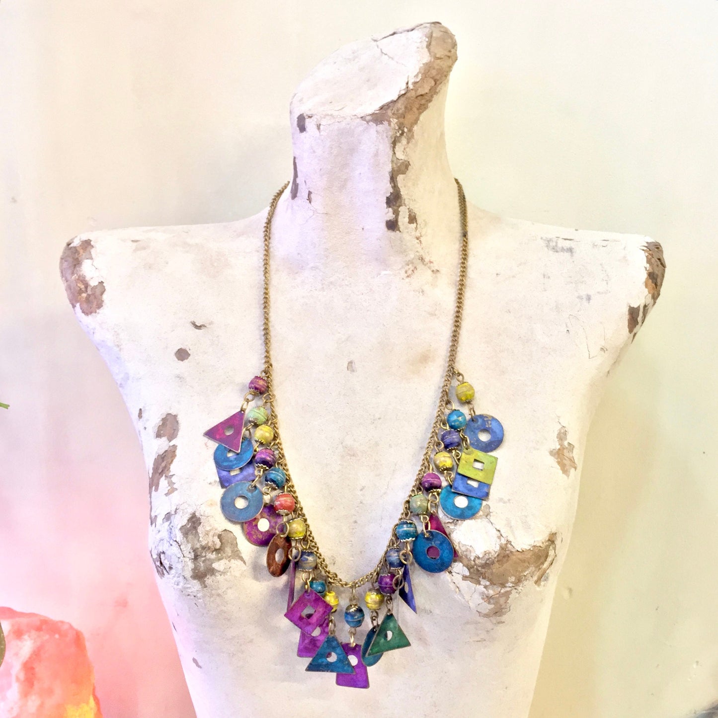 Vintage charm necklace with colorful metal beads, dangling ornaments, and gold chain, displayed on white mannequin bust. Unique costume jewelry piece, perfect for a holiday gift.