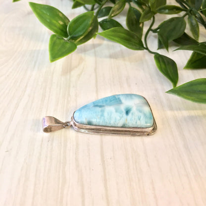 Vintage silver and larimar pendant necklace with blue and white natural stone, displayed on wooden surface with green leaves.