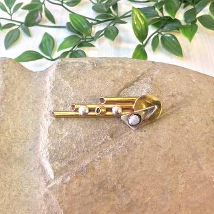 Vintage brass geometric abstract brooch pin featuring circles and triangles on a stone surface with greenery in the background.