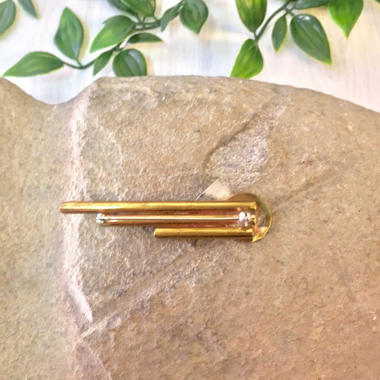 Vintage brass geometric abstract brooch pin featuring a circle and triangle design on a stone background with leaves.