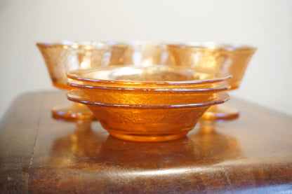 Set of three vintage orange carnival glass dessert dishes with an iridescent sheen, stacked on a wooden surface