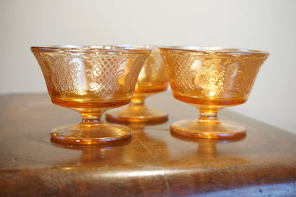 Set of three vintage orange carnival glass dessert dishes with an iridescent sheen, reflecting light and creating a beautiful glowing effect on a wooden surface.