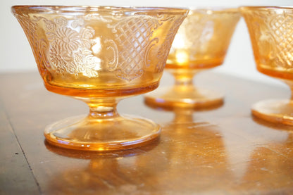 Ornate orange carnival glass dessert dishes with an iridescent sheen, reflecting light on a wooden surface.