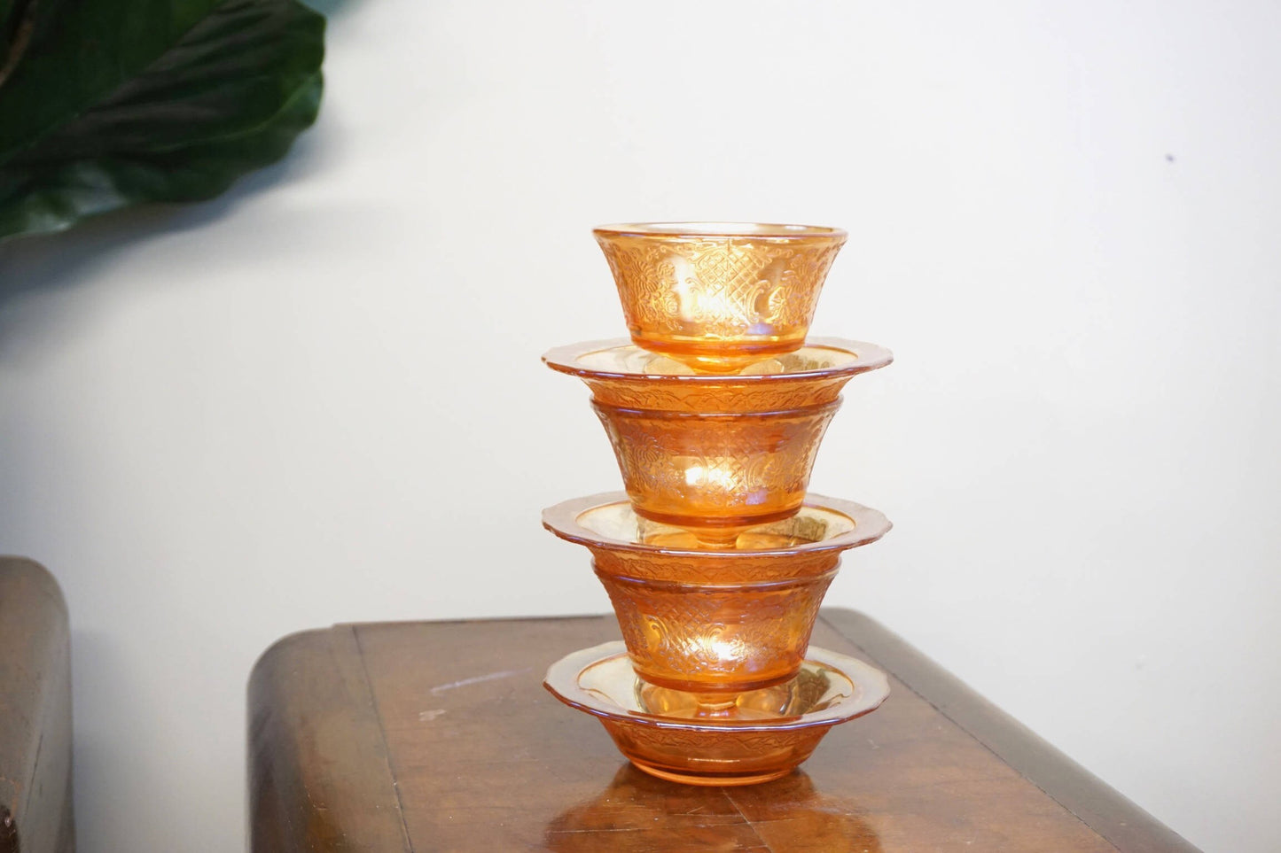 Set of three vintage orange carnival glass dessert dishes stacked on wooden table, showing iridescent sheen on textured glass surface.