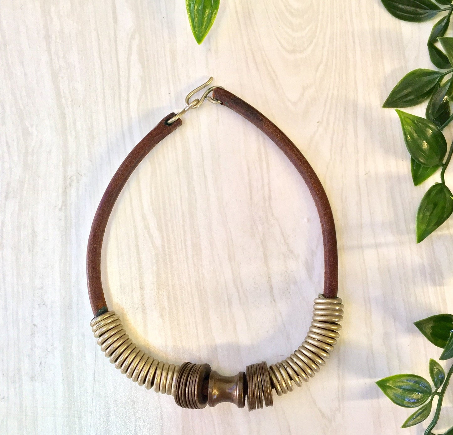 Vintage leather choker necklace with brass coil design on wooden background with green leaves, ethnic statement jewelry perfect for Mother's Day gift.