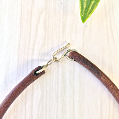 Vintage leather choker necklace with brass coil accent on wooden surface with green leaf, ethnic statement jewelry gift idea for Mother's Day