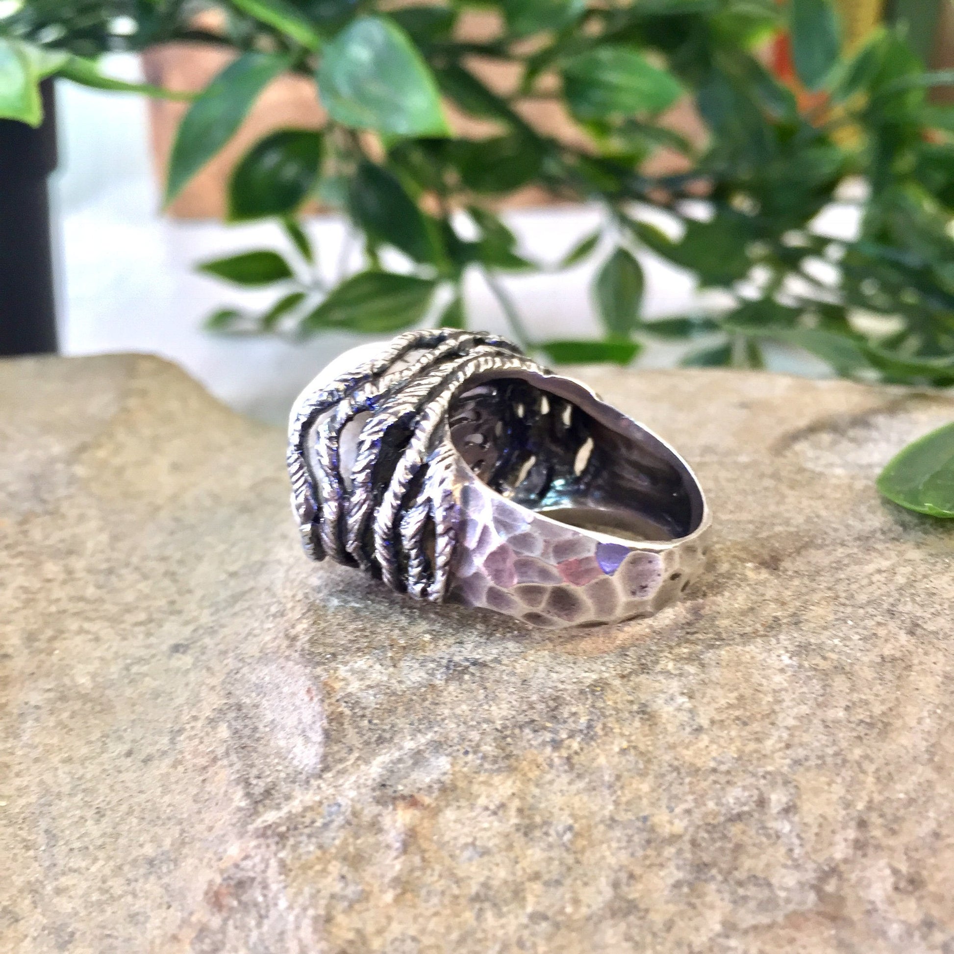 Vintage sterling silver ring with pink quartz stone in hammered rope setting on stone surface with green foliage in background