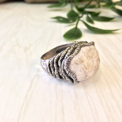 Vintage sterling silver ring with hammered rope design and large quartz stone, set against a light wooden background with green leaves.