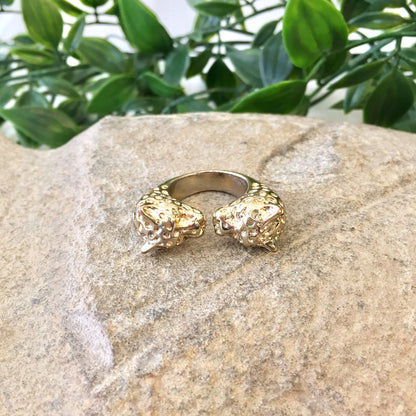 Vintage gold tone double leopard head statement ring displayed on stone with green plant leaves in background