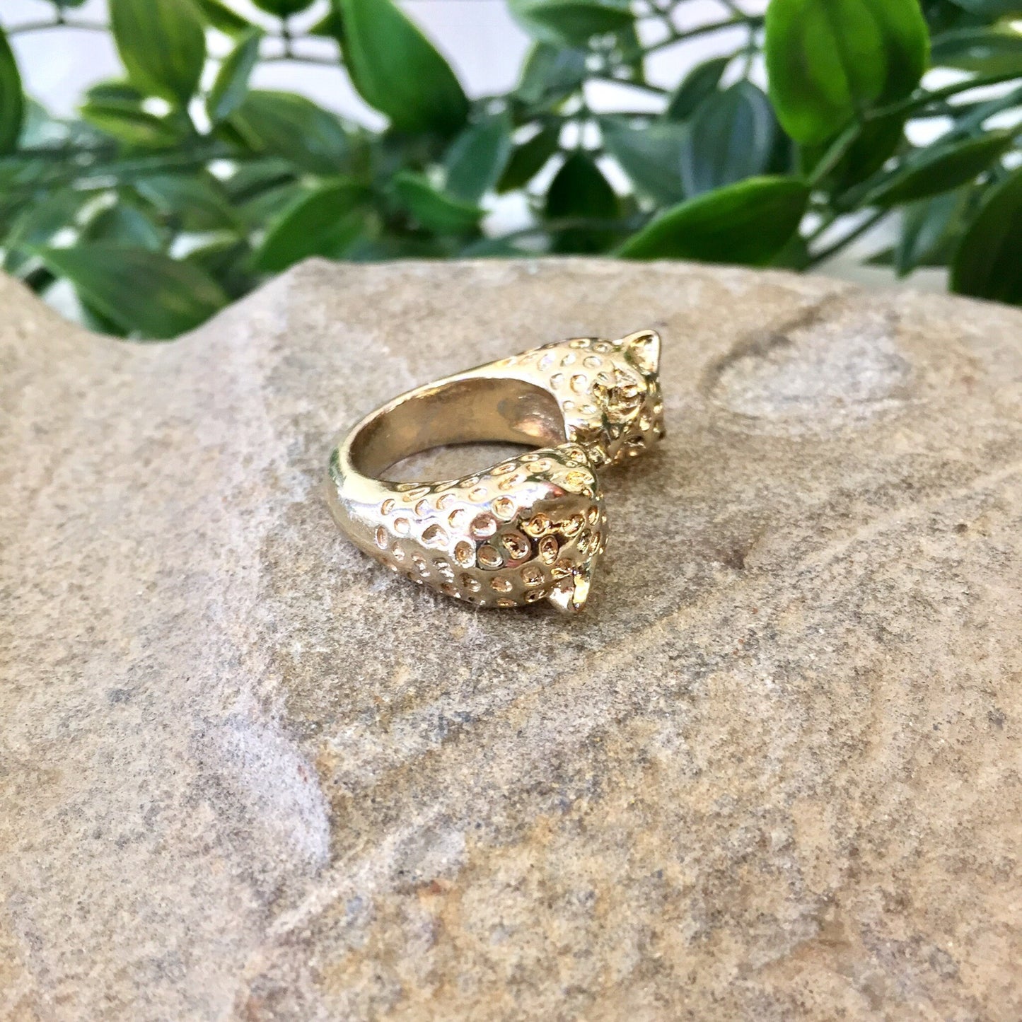 Vintage gold tone double leopard head statement ring displayed on stone surface with green foliage in background