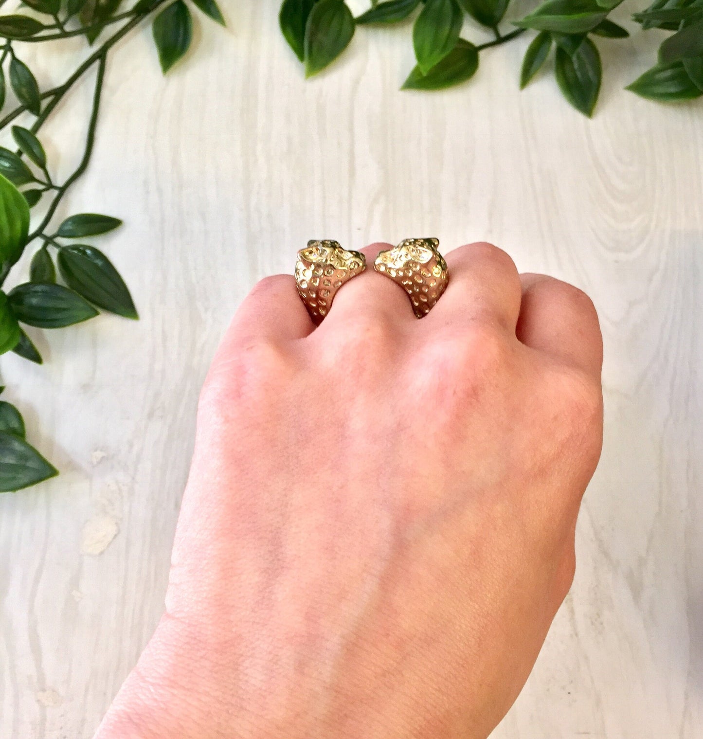 Vintage gold tone double leopard head statement ring on hand with greenery background