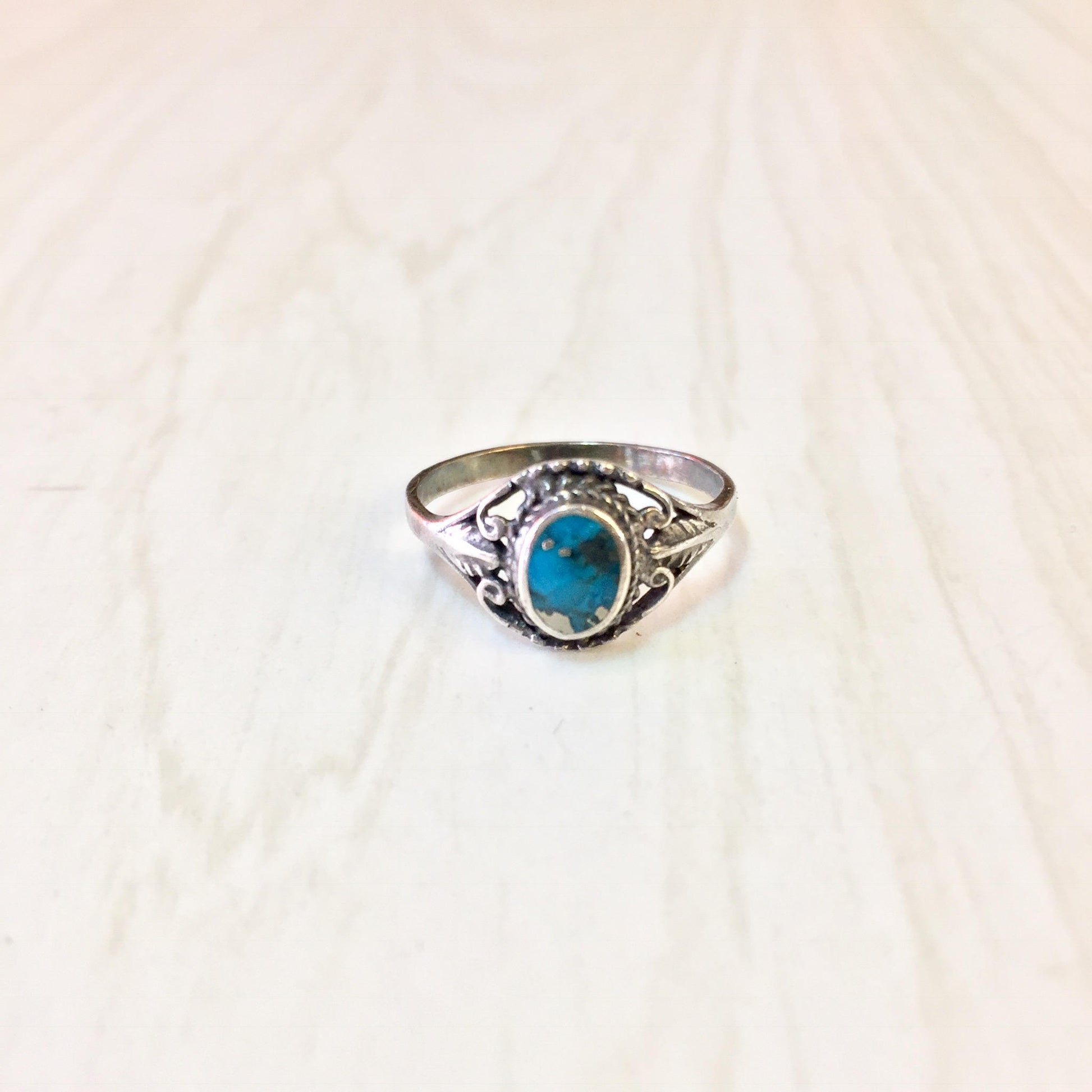 Vintage sterling silver ring with oval turquoise stone in ornate setting on light background