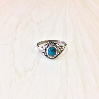 Vintage sterling silver ring with oval turquoise stone in ornate setting on light background