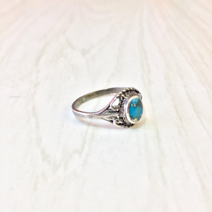 Vintage sterling silver ring with oval turquoise stone in ornate setting on light background