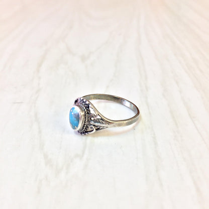 Vintage sterling silver ring with turquoise stone in ornate Southwestern style setting on light background