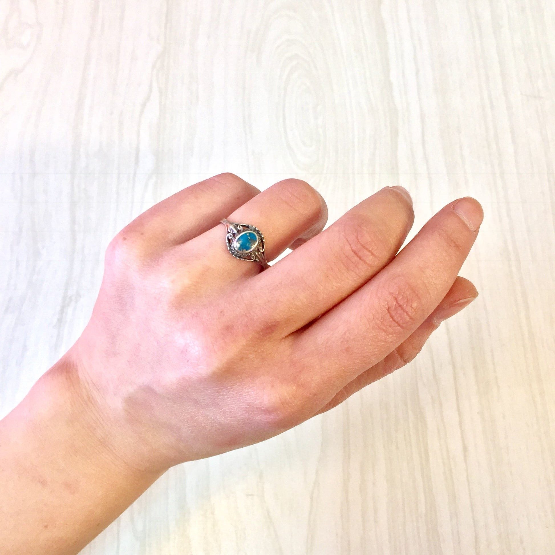 Vintage sterling silver ring with turquoise stone on a hand against a light wood background