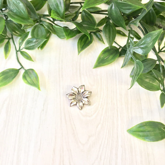 Vintage sterling silver flower brooch with detailed petal design, displayed on a wooden surface with green foliage accents for a nature-inspired presentation of vintage jewelry.