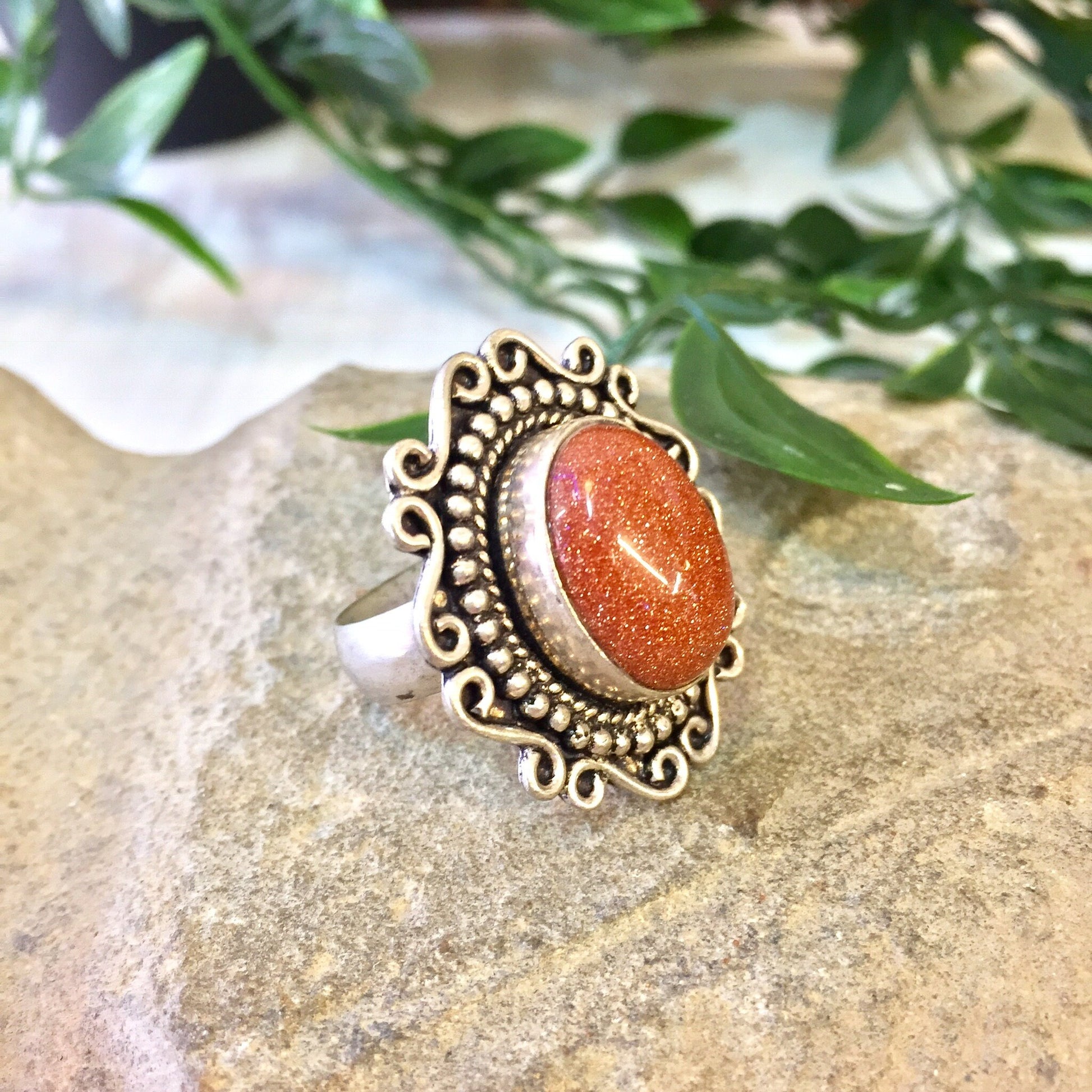 Vintage sterling silver ring with orange druzy quartz stone and intricate Celtic design on textured stone surface with greenery in background