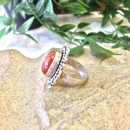 Vintage sterling silver ring with orange druzy quartz stone and intricate Celtic design on a textured gold background with greenery