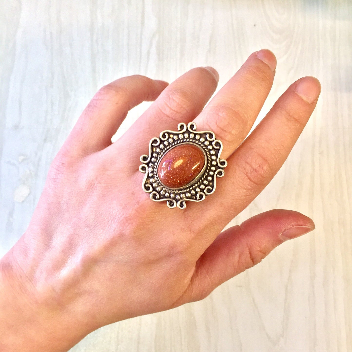 Vintage silver statement ring with orange druzy quartz gemstone and ornate Celtic design on a hand, showcasing the sparkly, eye-catching jewelry piece against a light wooden background.