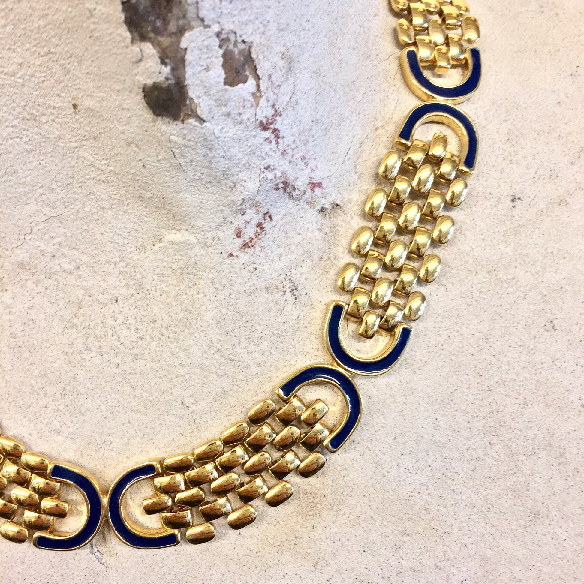 Vintage gold-tone chain link statement necklace with dark blue accents on textured beige background