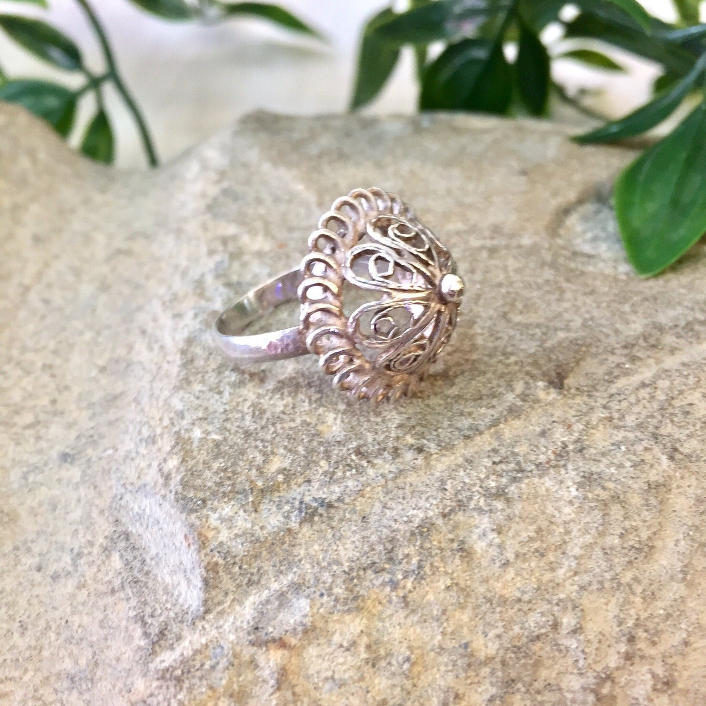 Vintage sterling silver dome ring with intricate cut-out design, placed on stone surface with greenery in background, perfect for weddings or as a Mother's Day gift.