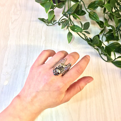 Vintage sterling silver eagle and skull statement ring on hand next to leafy green plant, biker jewelry