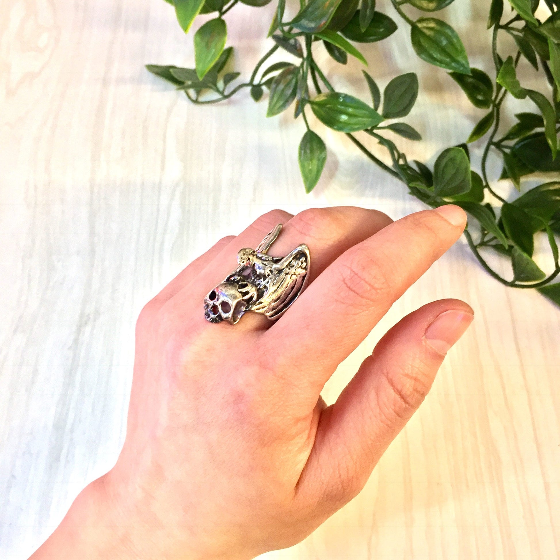 Vintage sterling silver eagle and skull biker ring on hand with plant in background