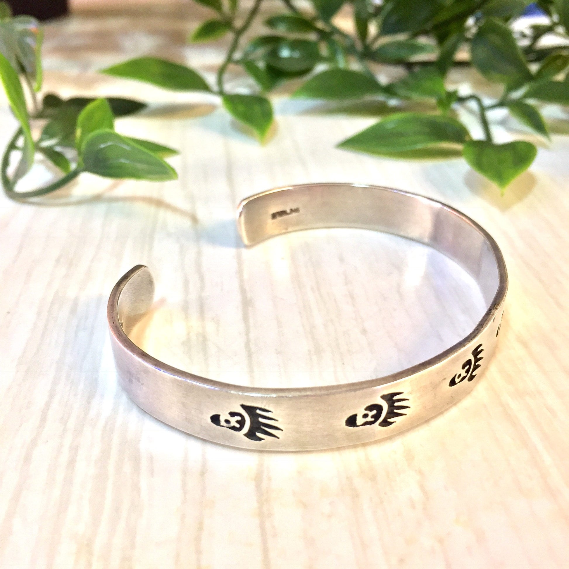 Vintage silver cuff bracelet with bear paw design, displayed on a wooden surface with green foliage in the background.