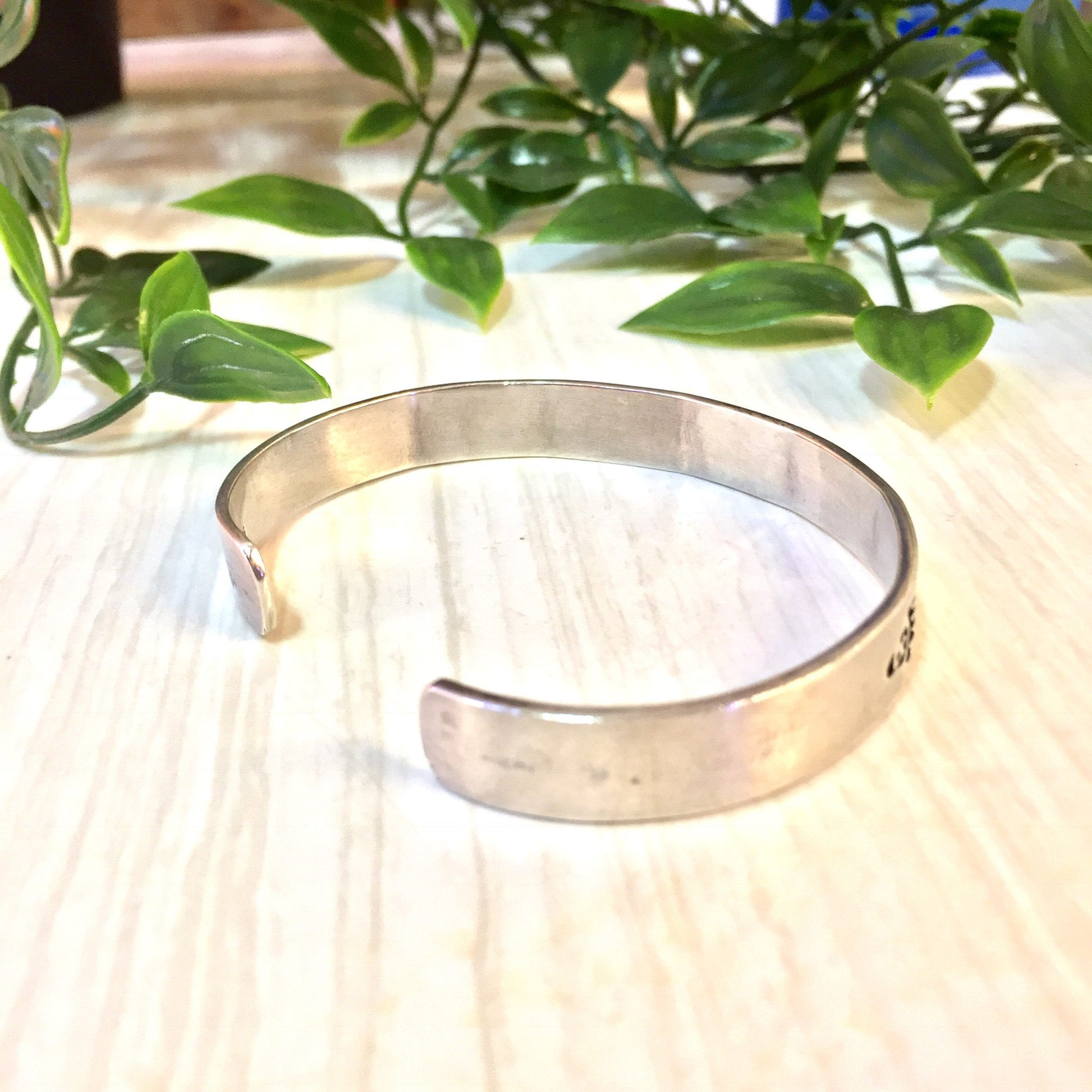 Vintage silver cuff bracelet with bear paw design, shown on wood surface with green foliage in background.