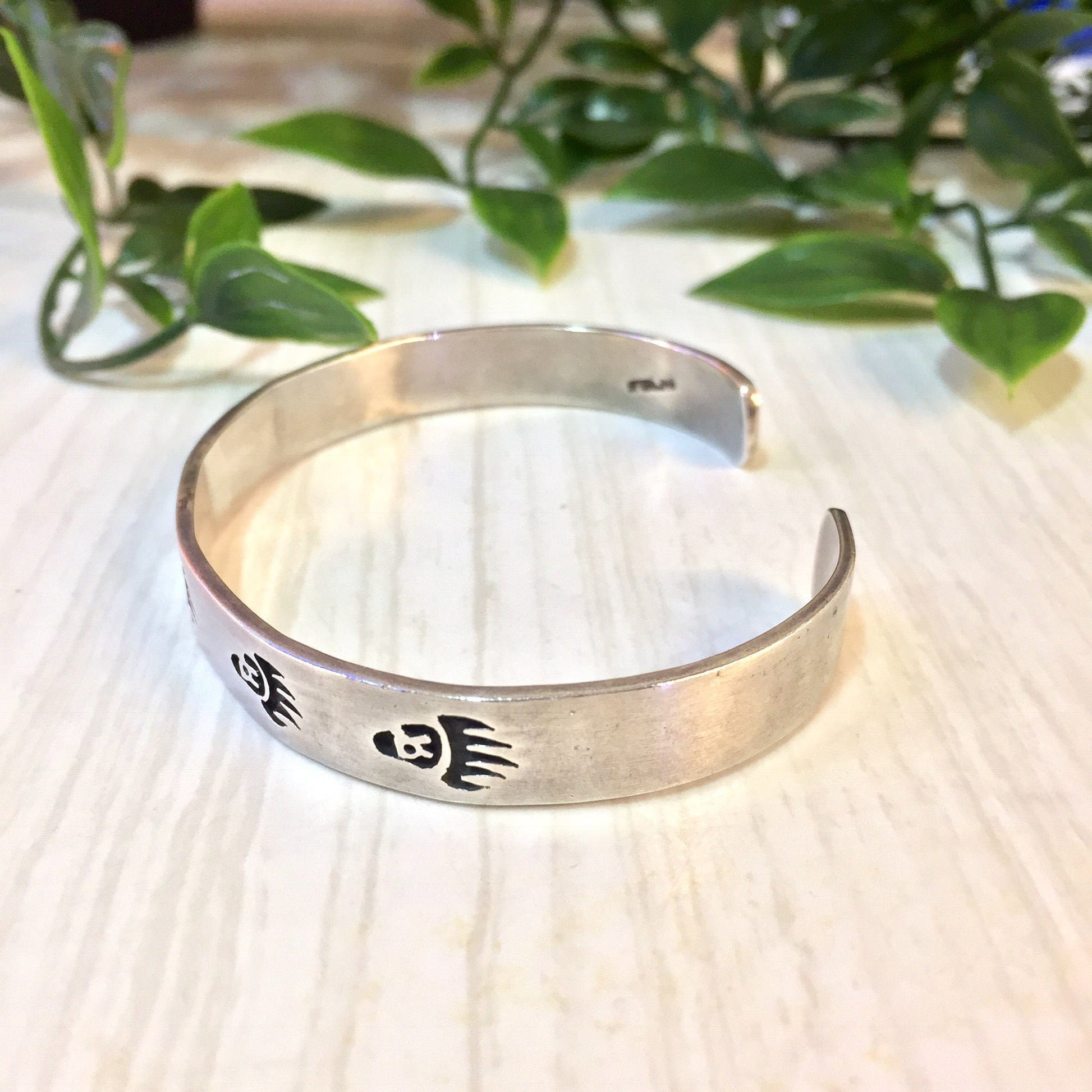 Vintage silver bear paw cuff bracelet displayed on wooden surface with greenery in background