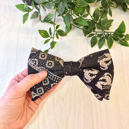 Vintage black patterned clip-on bow tie held in hand above green foliage, suitable as a gift for Father's Day or any dapper dad who appreciates retro menswear accessories