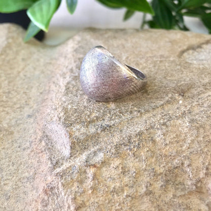 Vintage textured sterling silver pinky ring on stone background with green plant