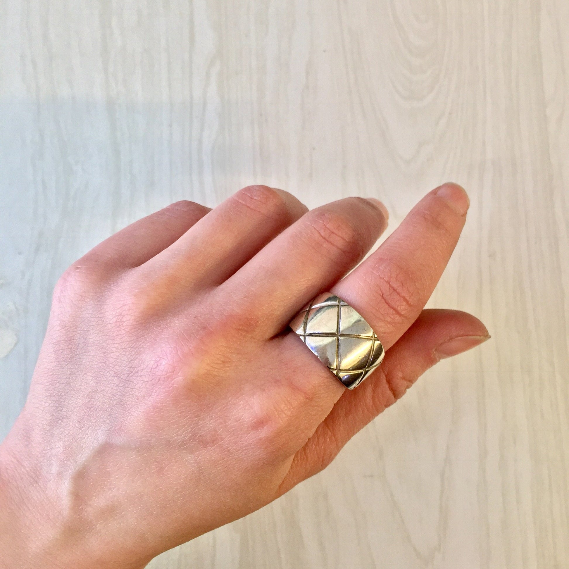 Vintage sterling silver thick band ring with X design and diamond pattern, held in a hand against a light wood background.