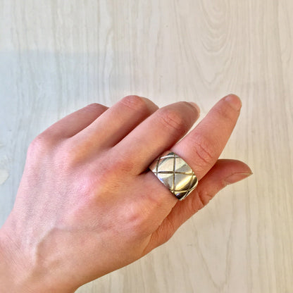 Vintage sterling silver thick band ring with X design and diamond pattern, held in a hand against a light wood background.