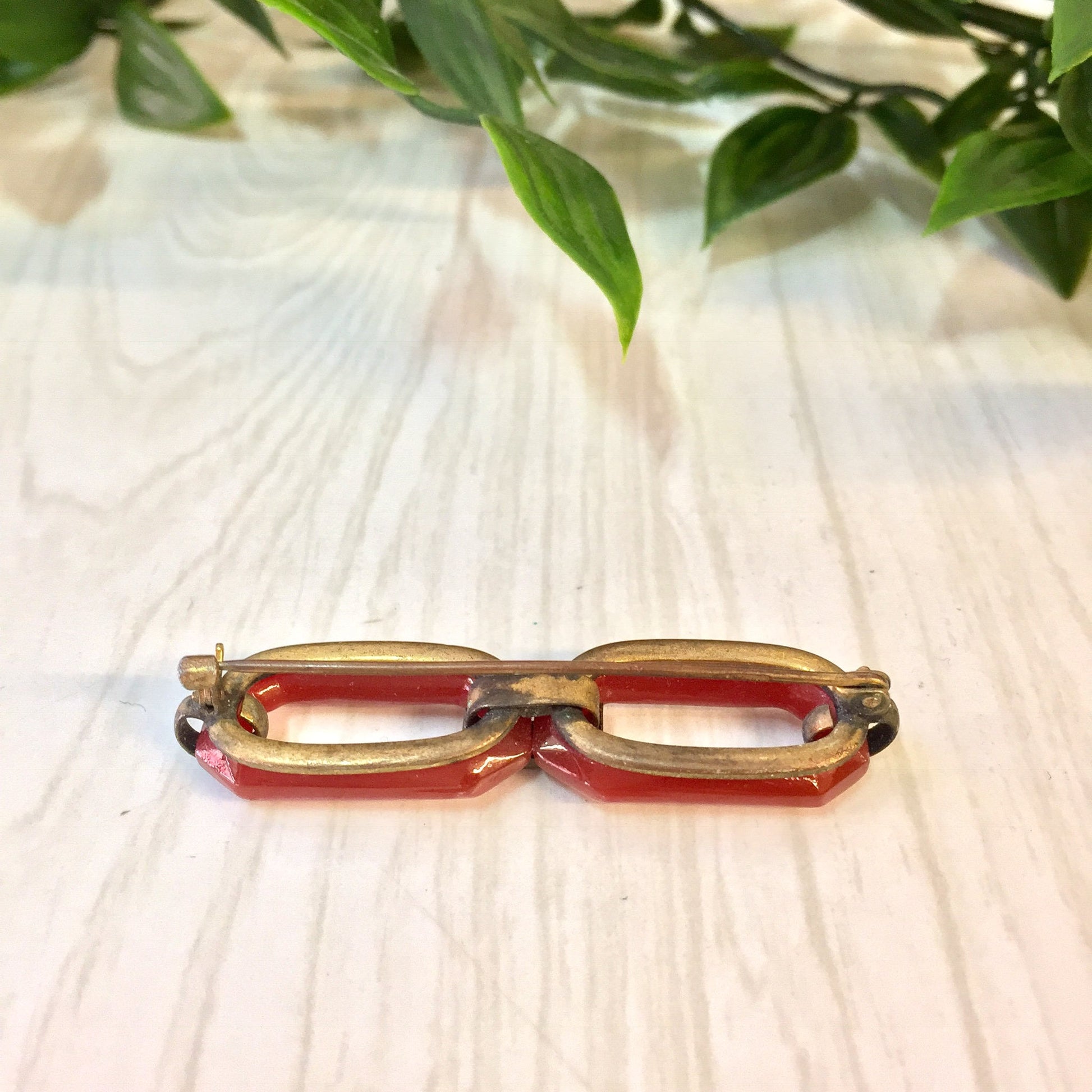 Vintage red and white carnelian brooch pin resting on light wooden surface with green foliage in background