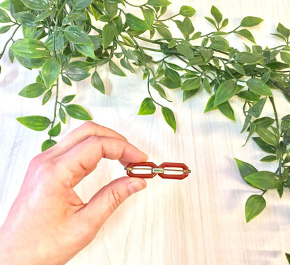 Woman's hand holding a vintage red brooch made of carnelian against a background of green leaves on a white cloth surface.