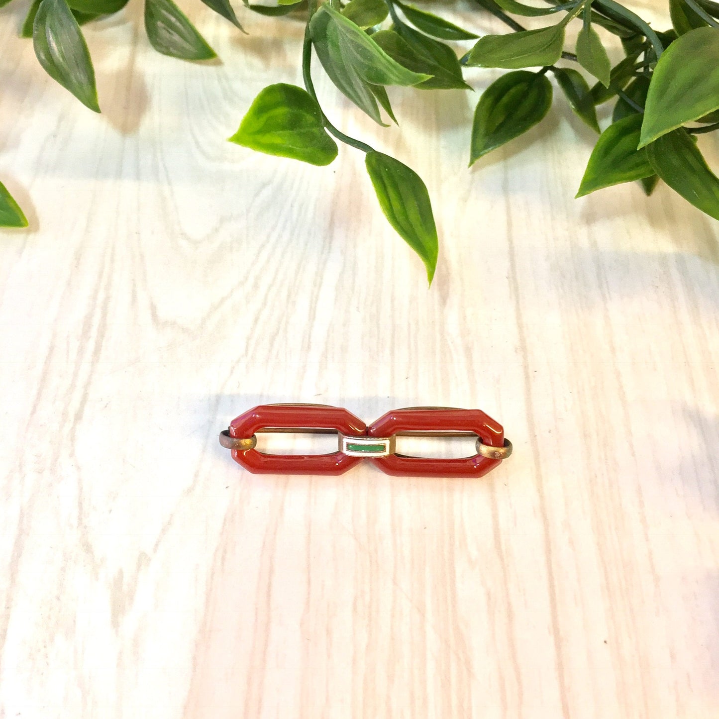 Vintage red and white carnelian brooch pin resting on light wooden surface with green leaves in background