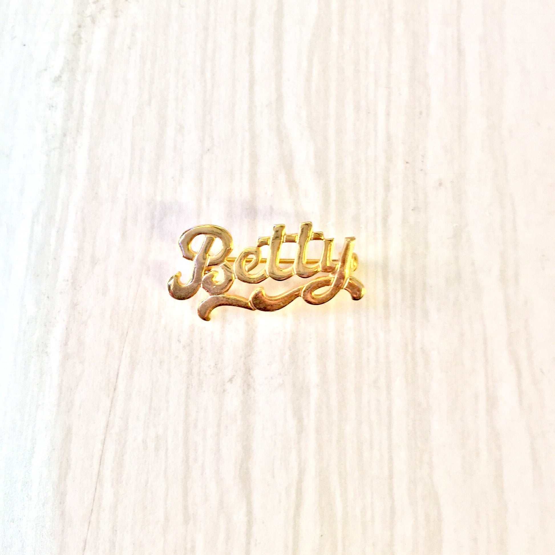 Vintage gold toned "Betty" name brooch pin on white wood background