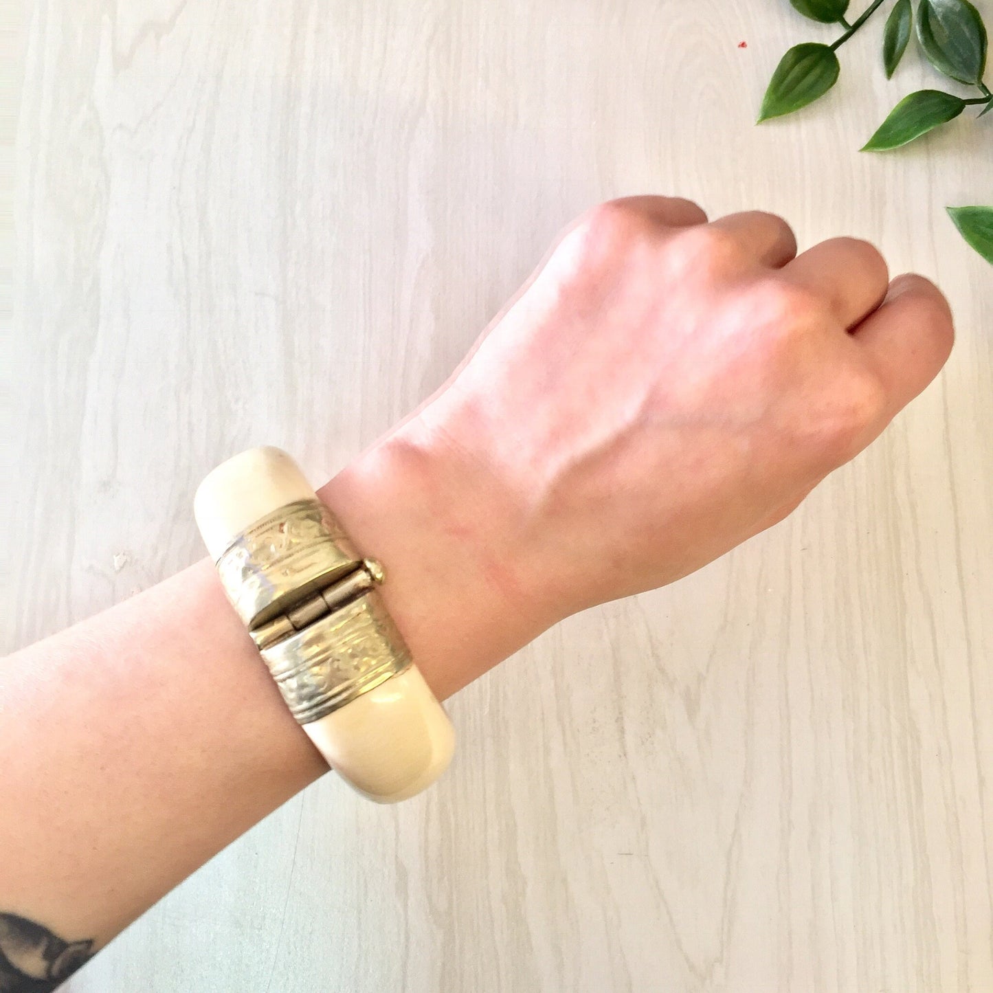 Vintage gold tone hinged bangle bracelet on wrist against light wood background with green leaves