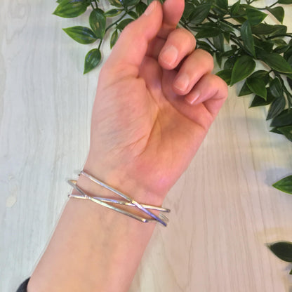 The image shows a hand wearing three interlocking silver bangle bracelets with a hexagonal geometric design, held against a wooden surface with a green plant in the background. The bracelets appear to be vintage sterling silver jewelry.